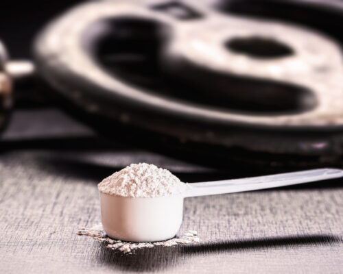 Imagem mostra um "scoop" cheio de creatina ao lado de anilhas de peso para exemplificar os benefícios da creatina no treino.