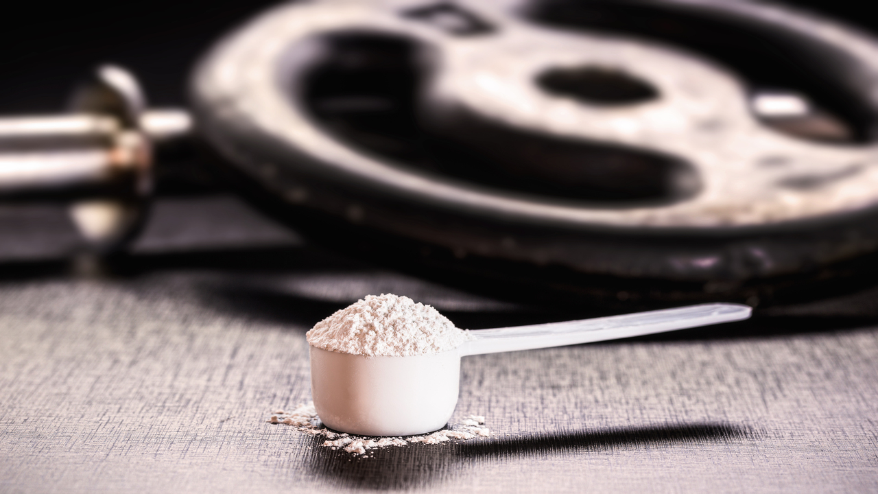 Imagem mostra um "scoop" cheio de creatina ao lado de anilhas de peso para exemplificar os benefícios da creatina no treino.